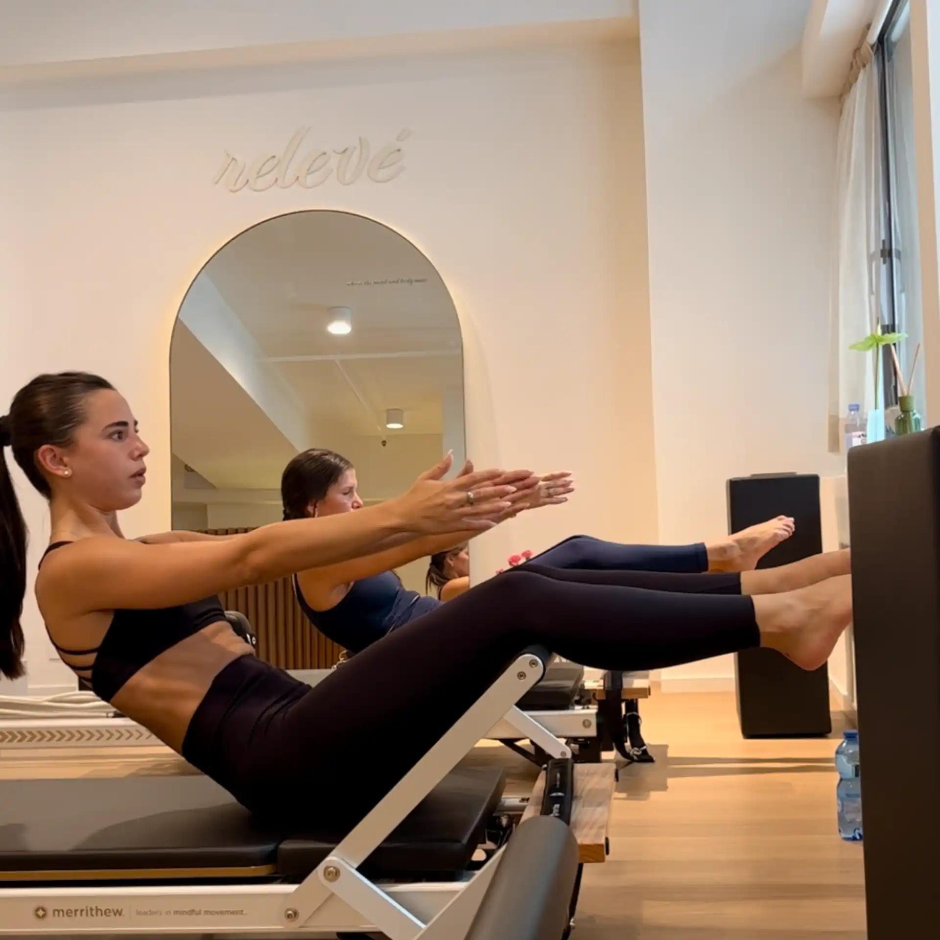 Two clients training on reformers under the Relevé wordmark at Relevé Pilates Studio Sheung Wan Hong Kong